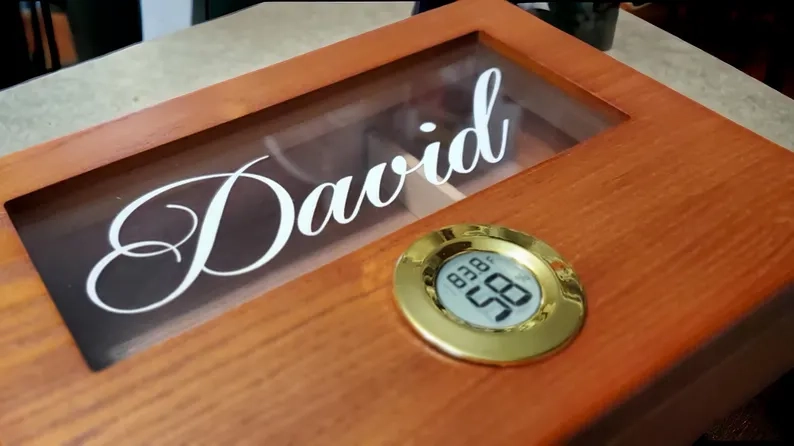 How to store cigars: a cedar humidor with a glass top and a front hygrometer, engraved with a name